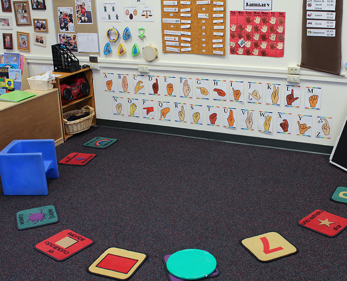 The circle time area of a classroom with 10 placemats for the children to sit on.  The sign language alphabet are taped to the wall along with other classroom routines.