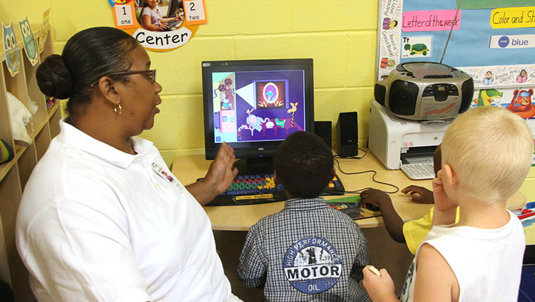 Caregiver and three children are looking at a computer screen with children's content in a caregiver setting.