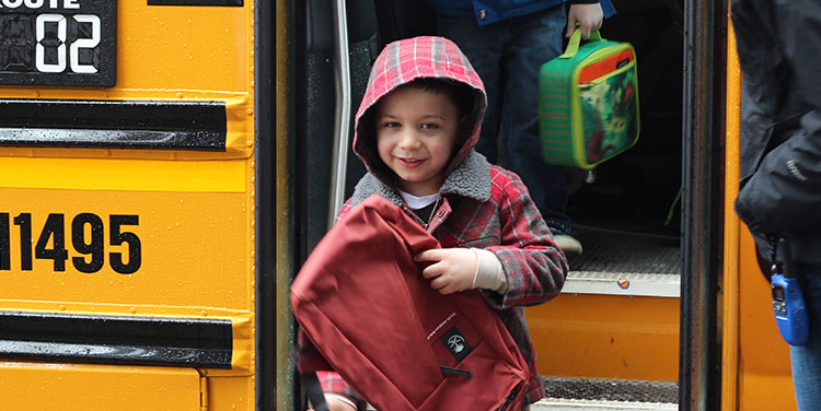Close up of Kindergarten boy leaving yellow school bus.